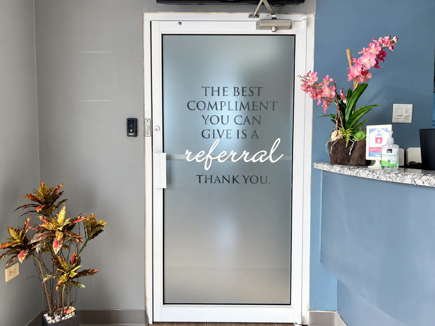 The frosted glass door beside the Elite Smiles front desk, with a referral thank-you message and pink orchids